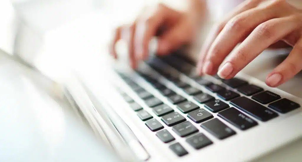 Une personne écrit sur un clavier d'ordinateur portable, on ne voit que ses mains